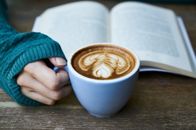 Imagen de una persona con café y leyendo un libro